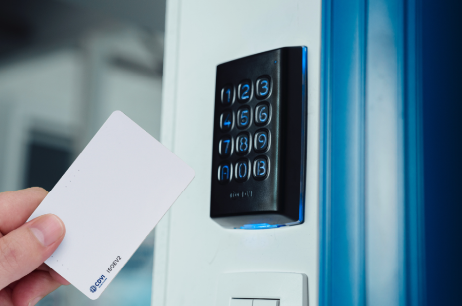 A black keypad is mounted on a white wall as an outstretched hand presents a white access card credential to it