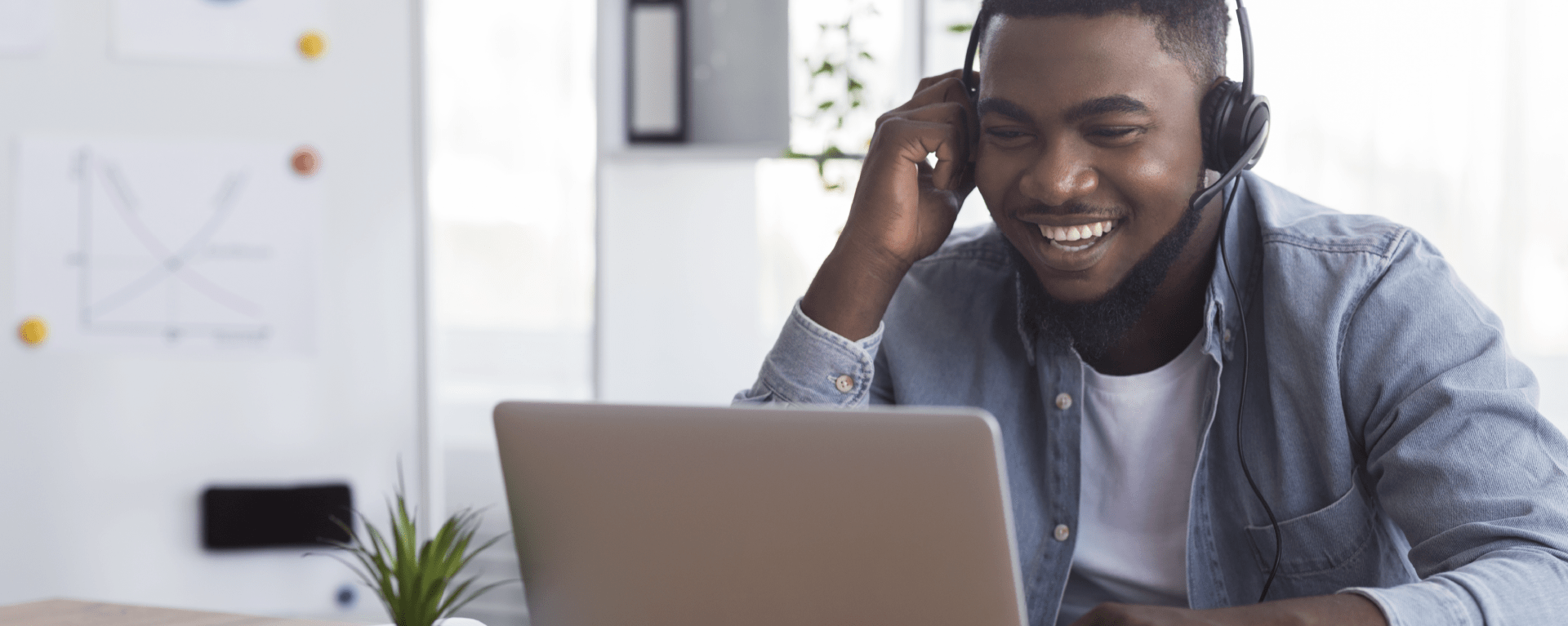 Book a Demo | Man sitting at laptop with headphones headset on, smiling and laughing at the screen