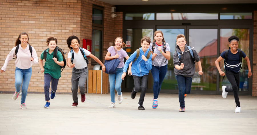 Group of children running and smiling away from a school entrance
