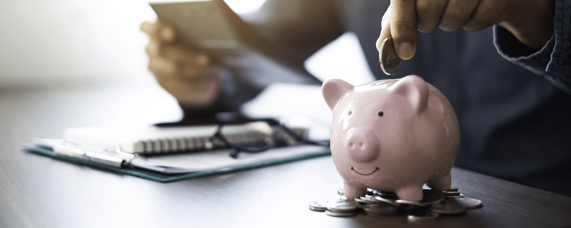 A closeup of a man dropping a coin into a pink piggybank to signify saving money