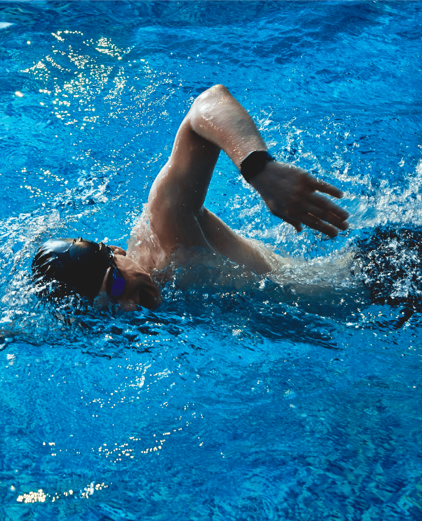A man swimming in a pool doing frontcrawl with his left arm out of the water in mid stroke