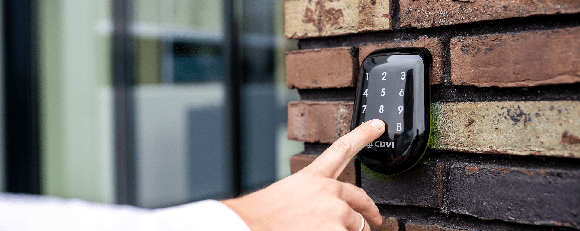 black CDVI keypad mounted on brick wall with hand outstretched